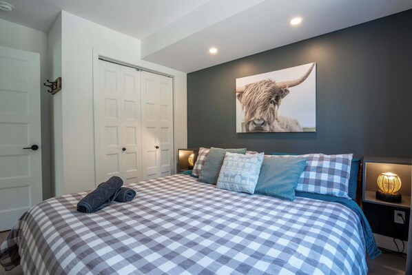 A bedroom with a checkered bedspread, a mounted artwork of a bull, and bedside lamps.