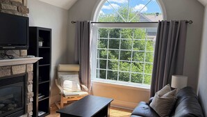 Un salon moderne avec une cheminée en pierre, un canapé en cuir noir, une table basse en bois et une grande fenêtre avec des rideaux.