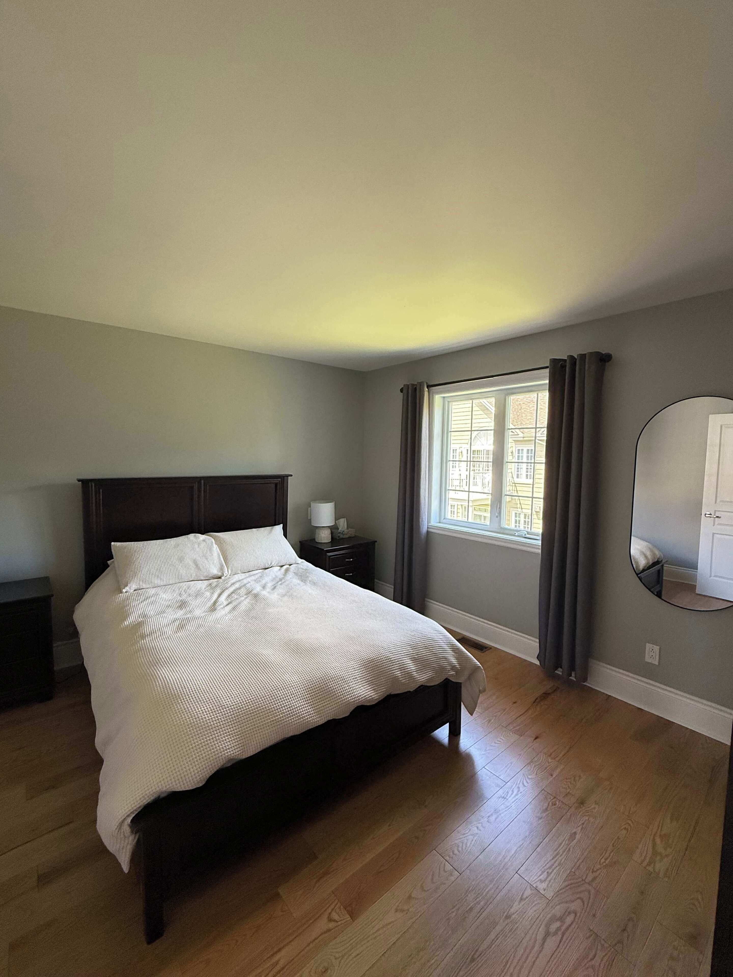 Une chambre à coucher avec un lit, une table de chevet, une fenêtre avec des rideaux et un miroir au mur.