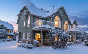Une maison à deux étages, dotée d’un porche et d’un balcon, tous deux abrités, et entourée de neige.