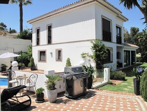 A two-story house with a patio area featuring a grill, outdoor seating, and a pool.