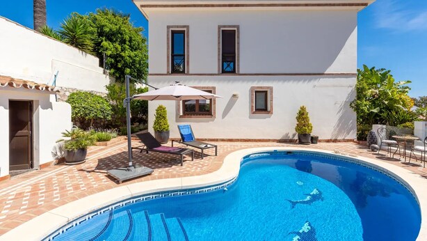 En swimmingpool med fliseterrasse, to liggestole og et lille bord.