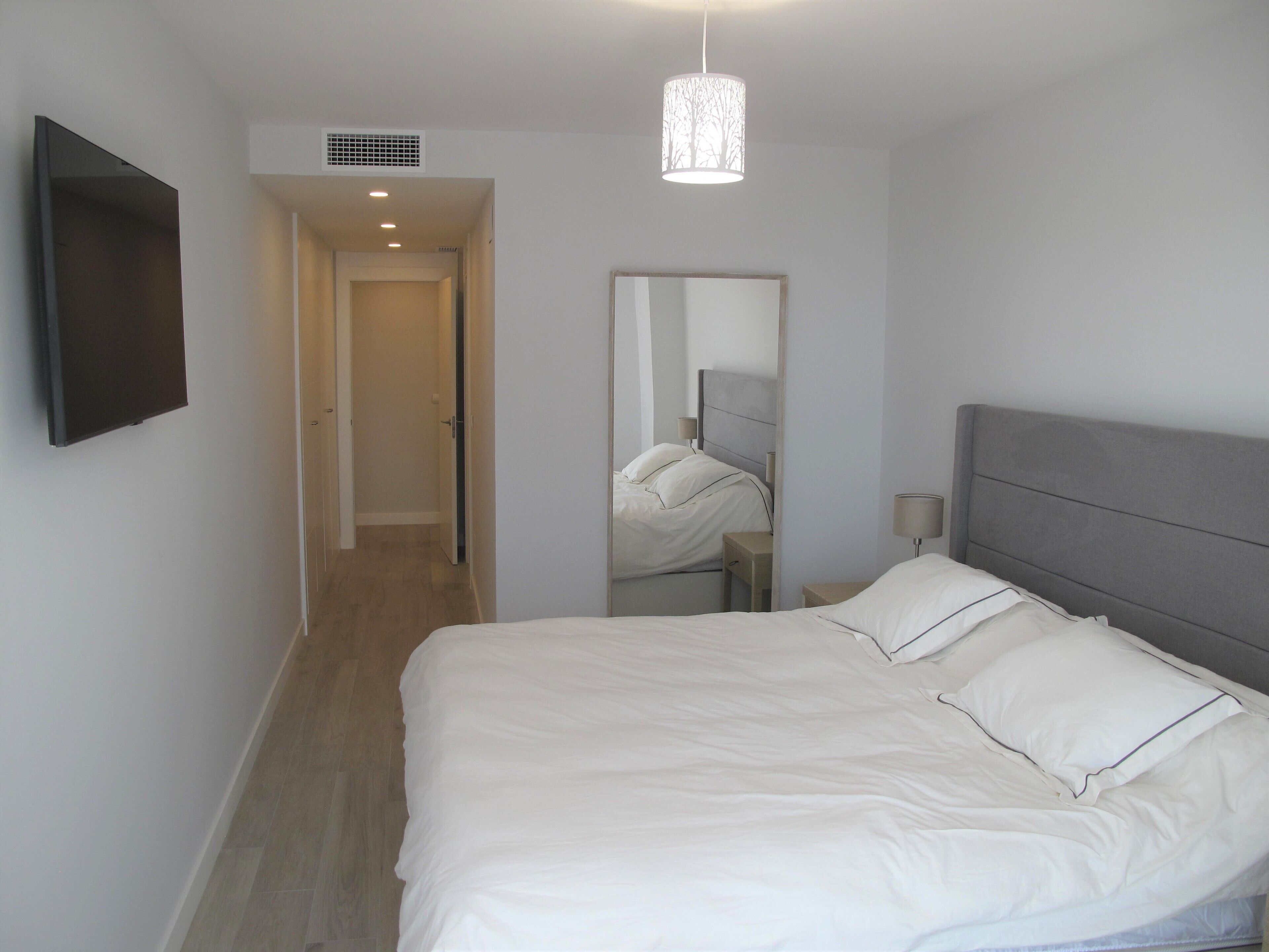 A bedroom with a bed, a flat-screen TV, a mirror, and a ceiling light fixture.