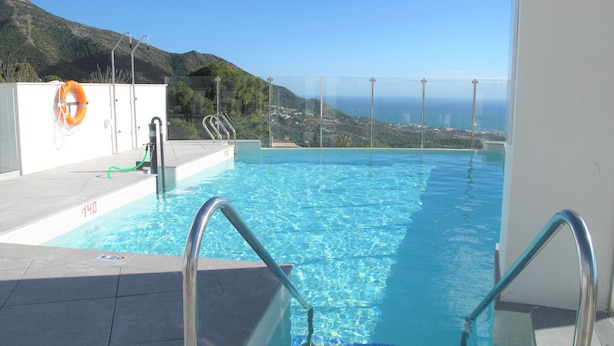 An infinity pool with clear blue water, metal railings, and a view of a mountainous landscape. - Holiday apartment in Inbisa (Mijas)