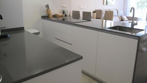 A modern kitchen with a central island, a built-in sink, and a dining area with chairs and a sofa. - Holiday apartment in Inbisa (Mijas)