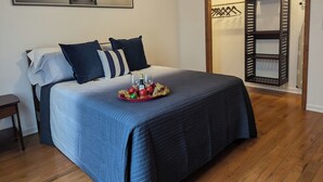 Ein ordentlich bezogenes Bett mit einer blauen Steudecke, ein Tablett mit Gläsern und einer Flasche sowie ein Landschaftsbild an der Wand.