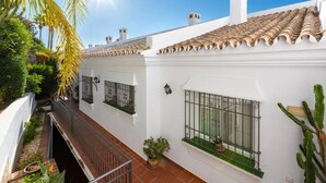 Un bâtiment blanc avec des tuiles de terre cuite sur le toit, un petit balcon doté d’une rambarde en métal et des plantes en pot.