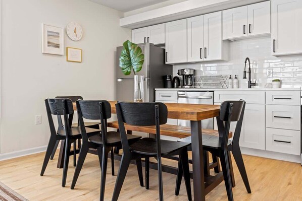 A modern kitchen with white cabinets, a wooden dining table, and black chairs.
