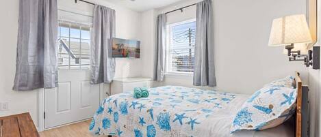 A bedroom with a bed, a bedside table, a lamp, and a window with curtains.