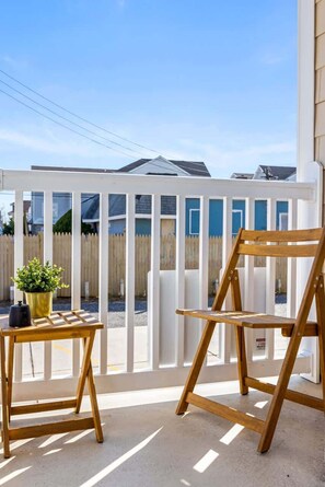 Eine Holzterrasse mit weißem Zaun, einem kleinen Tisch mit Topfpflanze und einem Holzstuhl.