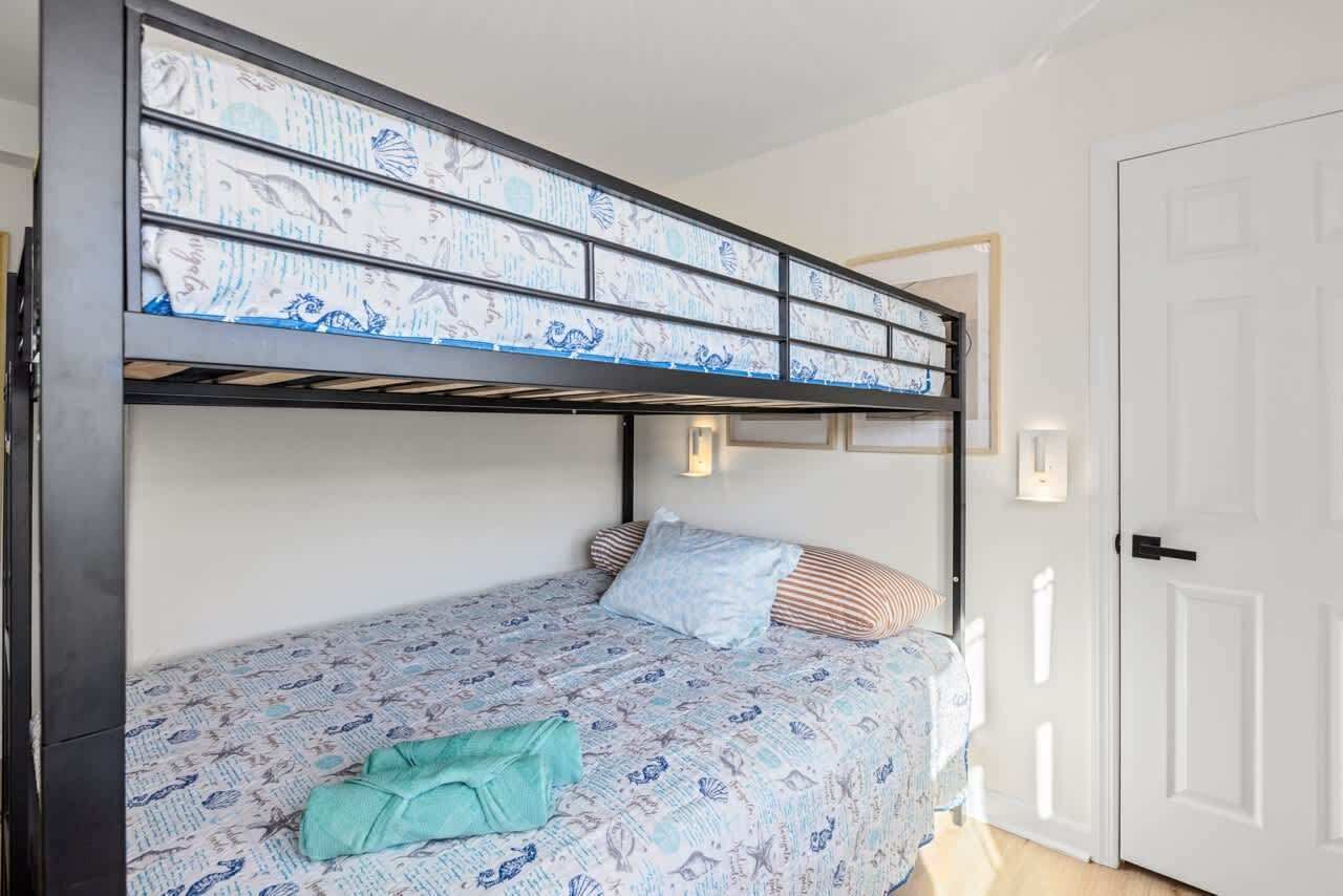 A bunk bed with a patterned bedspread, a single pillow, and a folded blanket on the lower bunk.