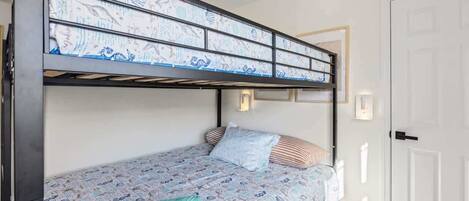 A bunk bed with a patterned bedspread, a single pillow, and a folded blanket on the lower bunk.