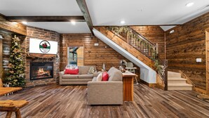 A cozy living room with a fireplace, a sofa, and a staircase leading to an upper level. - Resort Cabin Near Branson Attractions & Thunder Ridge (Hollister)