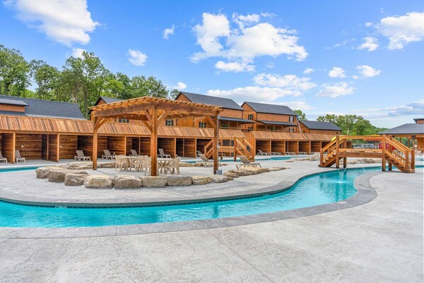 A pool area with wooden structures, lounge chairs, and a clear blue sky.
