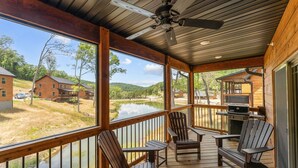 A wooden deck with Adirondack chairs and a grill, overlooking a lake and houses. - Resort Cabin Near Branson Attractions & Thunder Ridge (Hollister)