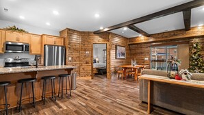 A modern kitchen with wooden cabinetry, a stainless steel refrigerator, and a bar area with stools. - Resort Cabin Near Branson Attractions & Thunder Ridge (Hollister)
