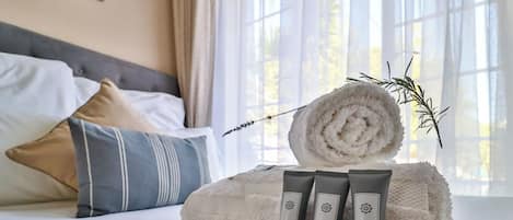 Una cama bien tendida con una toalla enrollada y dos botellas de loción corporal sobre una colcha estampada.