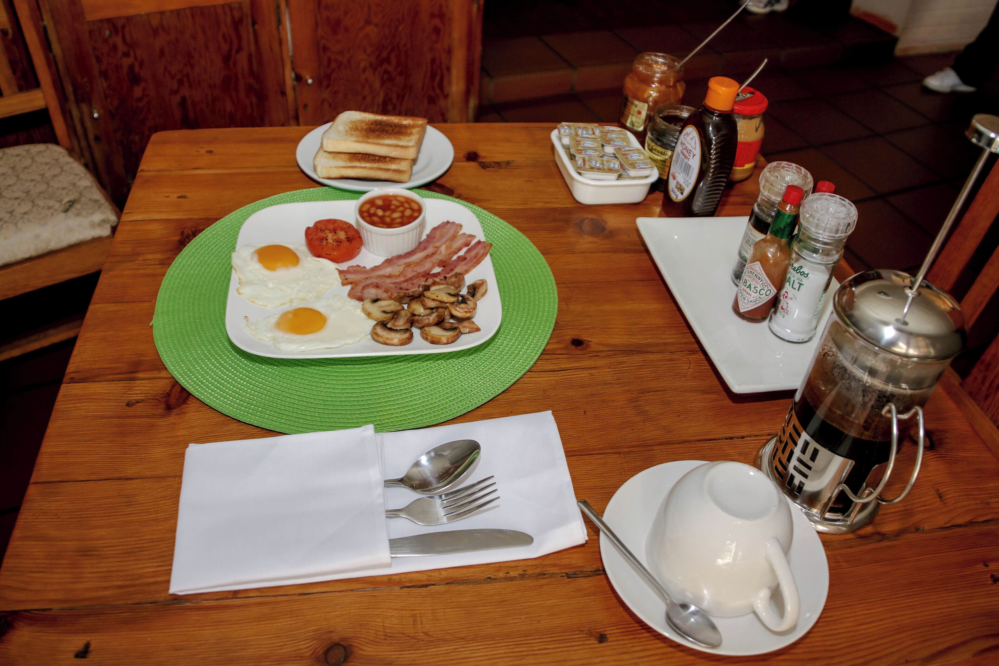 A breakfast setting with toast, eggs, bacon, mushrooms, and beans on a wooden table.