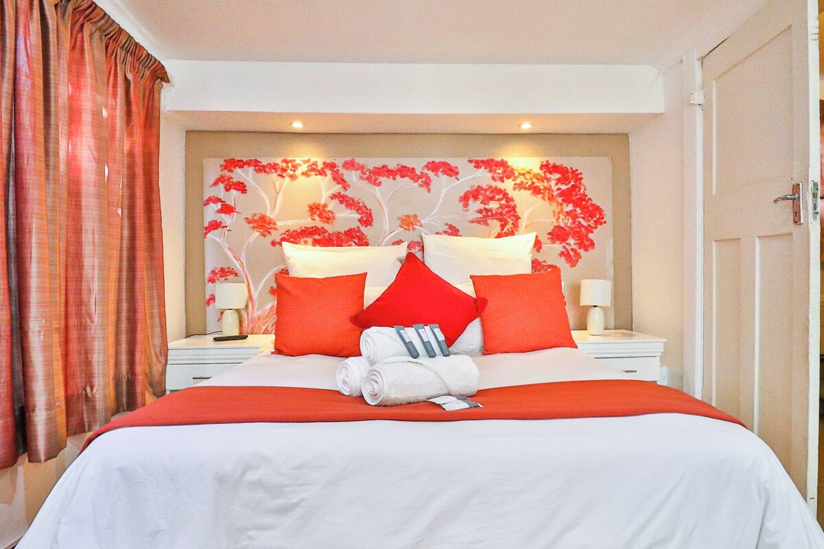 Ein Hotelzimmer mit einem großen Bett, rot-weiß gestreifter Bettwäsche, einem blumigen Kopfende und einem Nachttisch mit einer Lampe.