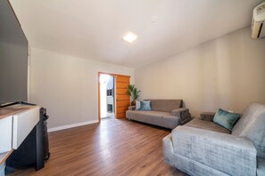 A spacious living room with hardwood flooring, a grey sofa, and a TV stand. - Casa alto padrão com piscina 15 pessoas (Bombinhas)