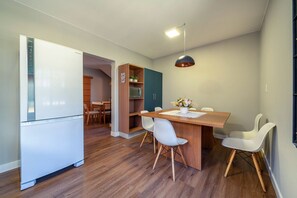 Une cuisine moderne avec un réfrigérateur blanc, des armoires en bois et un coin repas comprenant une table en bois et des chaises blanches.
