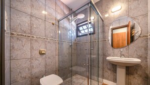 Un baño con ducha de vidrio, inodoro y lavamanos con espejo.