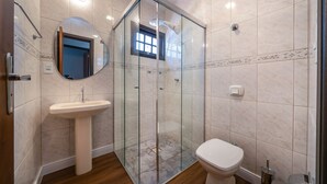 A bathroom with a glass-enclosed shower, a pedestal sink, and a toilet. - Casa alto padrão com piscina 15 pessoas (Bombinhas)