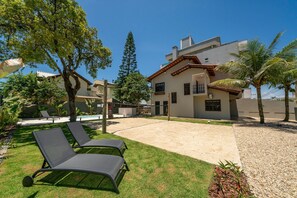 A residential area with a house, two lounge chairs, a small garden, and a pool. - Casa alto padrão com piscina 15 pessoas (Bombinhas)
