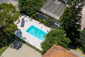 Eine Vogelperspektive auf einen Swimmingpool, umgeben von Bäumen und einem Gebäude mit einem Ziegeldach.