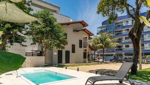 A swimming pool with lounge chairs, surrounded by buildings and trees. - Casa alto padrão com piscina 15 pessoas (Bombinhas)