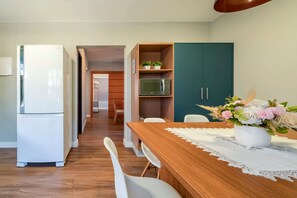 A modern kitchen with white appliances, a wooden dining table with chairs, and a green cabinet. - Casa alto padrão com piscina 15 pessoas (Bombinhas)