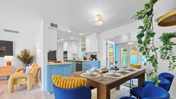 A modern kitchen with white cabinets, a wooden dining table, and blue chairs.