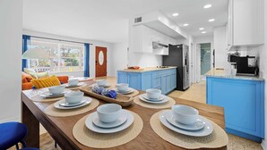 A modern kitchen with blue cabinets, a wooden dining table set with white plates and bowls, and a view of the outside through large windows.