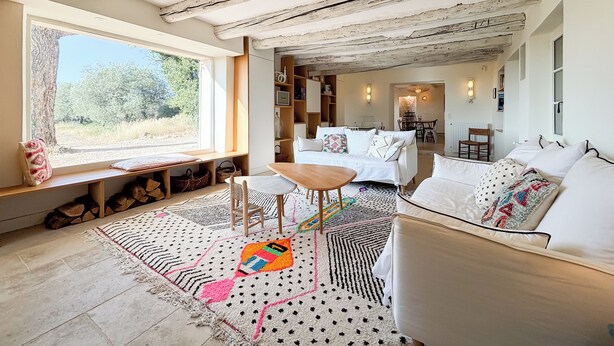 Ein gemütliches Wohnzimmer mit einem großen Fenster, Holzboden und einem Essbereich im Hintergrund.