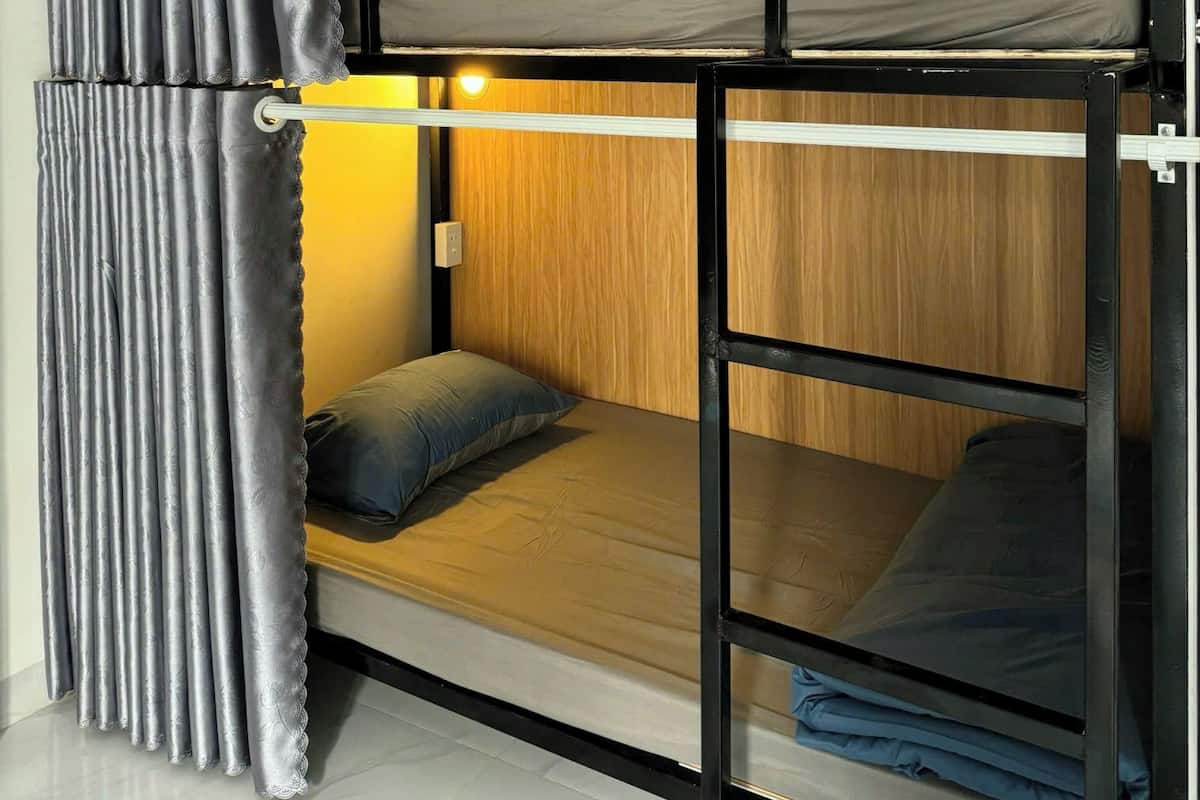 A bunk bed with a wooden headboard, a curtain, and a small bedside table with a lamp.