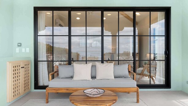 A room with a large window, a sofa, a wooden table, and a wooden cabinet. - Sophisticated Modern Home w/ Ocean Views, Gorgeous Master Suites & Private Jacuzzi (Las Catalinas)
