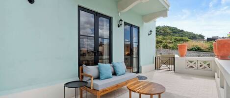 A balcony with a sofa, a small table, and a potted plant.