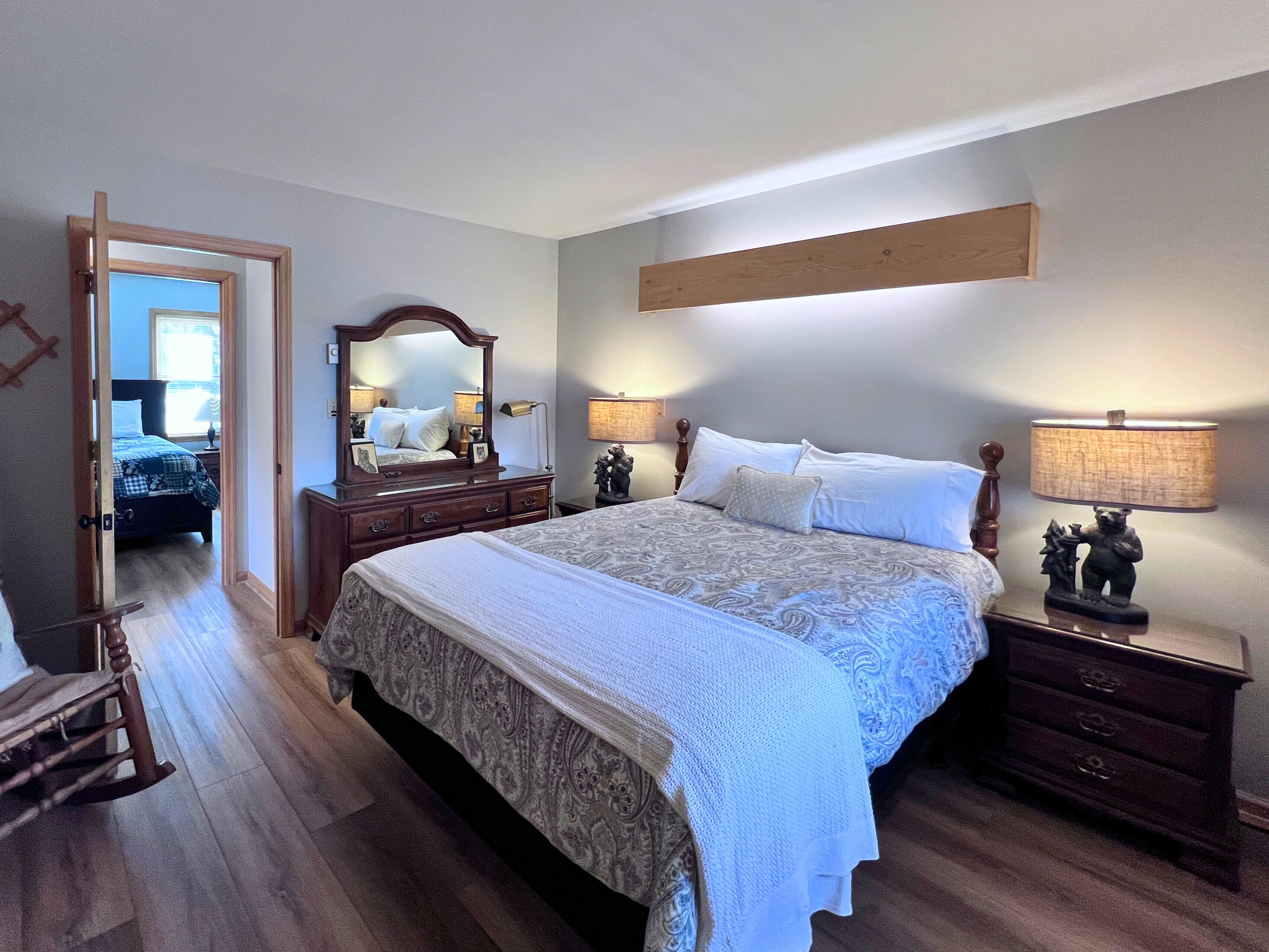A bedroom with a large bed, a dresser, a nightstand, and a mirror.