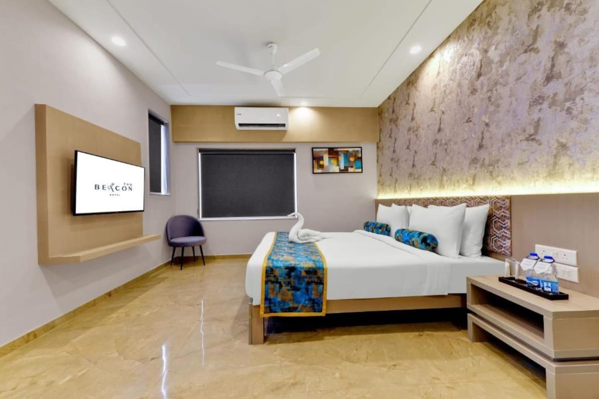 A hotel room with a bed, a chair, a TV, an air conditioner, and a ceiling fan.