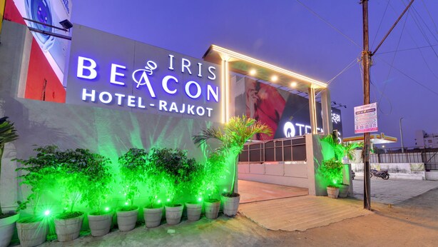 Außenansicht des Iris Beacon Hotels in Rajkot, mit beleuchteter Beschilderung und Topfpflanzen.