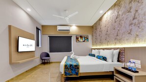 Ein modernes Hotelzimmer mit einem großen Bett, einem Flachbildfernseher, einem Deckenventilator und einer wandmontierten Klimaanlage.