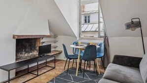 A cozy room with a fireplace, a dining table with chairs, a sofa, and a TV on a stand. - Lovely 1BR in The Heart of Latin Quarter (Paris)