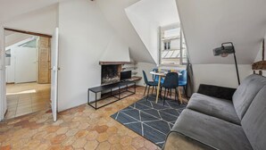 A cozy attic bedroom with a sloped ceiling, a fireplace, a bed, and a large window. - Lovely 1BR in The Heart of Latin Quarter (Paris)