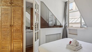 A bedroom with a wooden wardrobe, a bathroom with a shower, and a window with a view of buildings. - Lovely 1BR in The Heart of Latin Quarter (Paris)