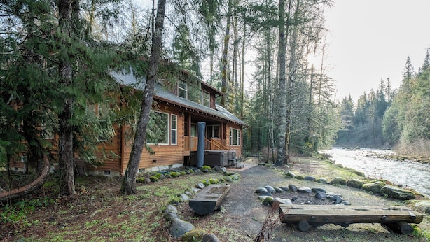 Une cabane en bois avec un porche, entourée d’arbres et bordée par une rivière.