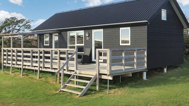 A small, dark-colored cabin with a wooden deck and a staircase leading to the entrance. - 5 Star Holiday Home in Lokken (Lokken)