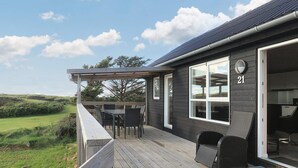 A wooden deck with outdoor furniture, a large window, and a view of the landscape. - 5 Star Holiday Home in Lokken (Lokken)