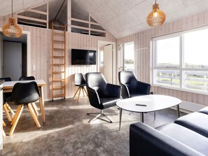 A modern interior with a wooden floor, a round table, and black leather chairs. There is a TV mounted on the wall and a ladder leaning against the wall.