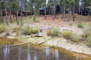 A cabin with a deck overlooking a forested area and a small stream.
