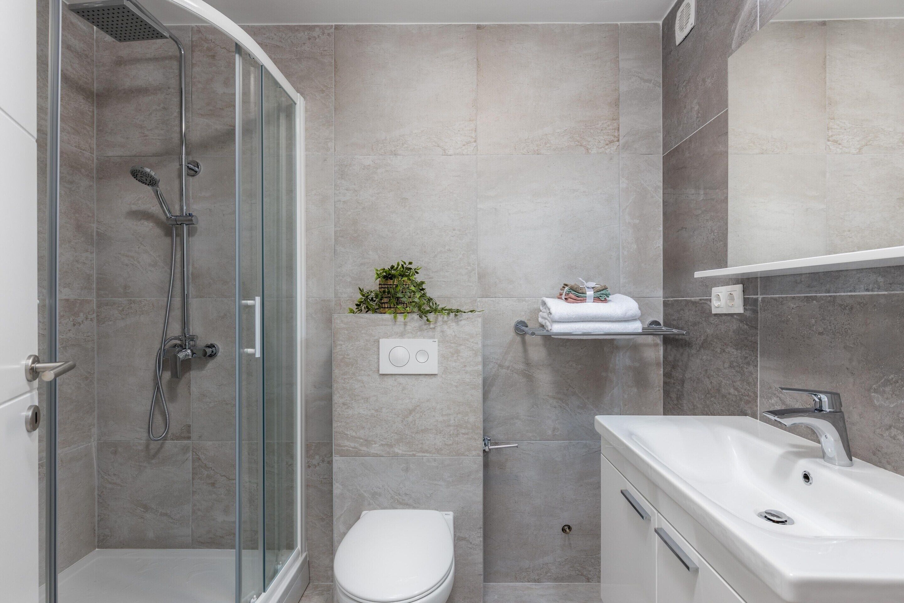 Un bagno moderno con cabina doccia in vetro, un water bianco e un lavandino bianco.